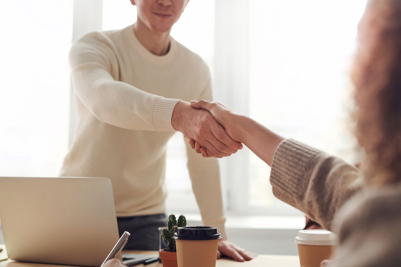 Two people shaking hands across a desk with an open laptop